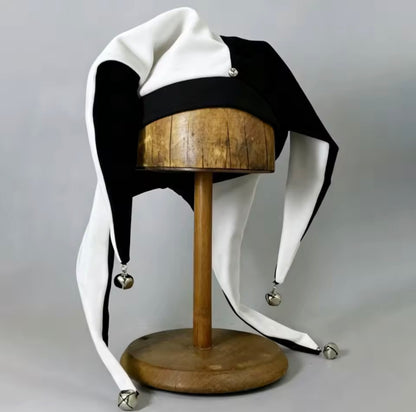 Black and white jester hat with silver bells, front view on wooden stand