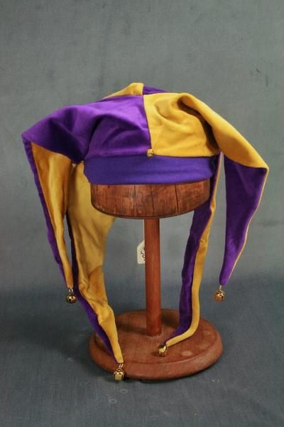 A purple and gold jester hat displayed on a wooden stand against a dark gray background.